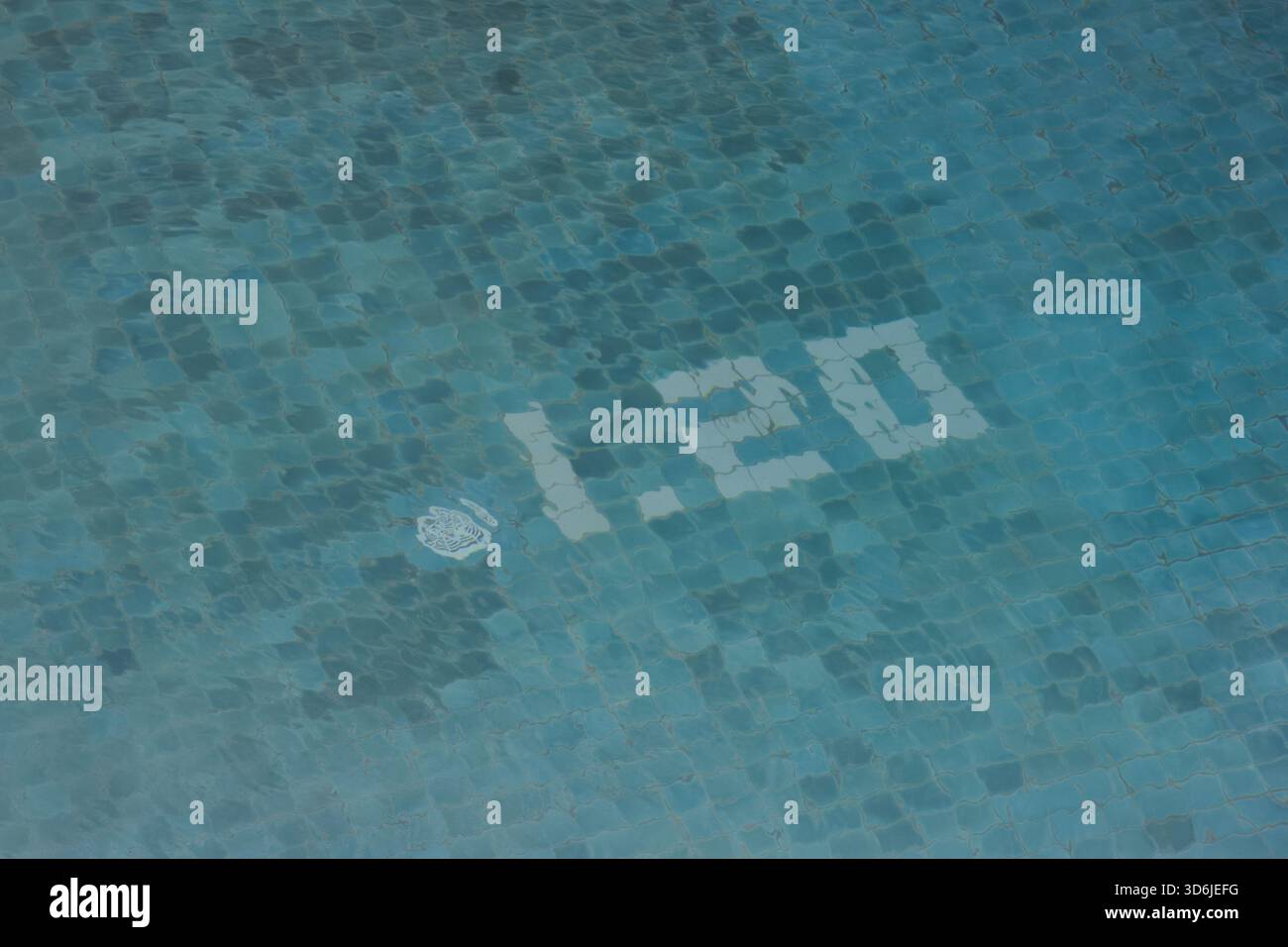 Ruhige blaue Wasseroberfläche des Swimmingpools mit Mosaikfliesenboden. Die Anzahl der Tiefenmarkierungen, die die Messung für die Sicherheit angibt, erzeugt ein ruhiges und friedliches fe Stockfoto