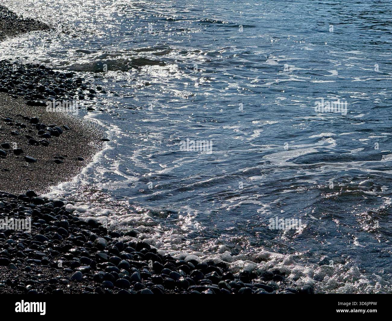 Sanfte Wellen am Kiesstrand am Abend Stockfoto