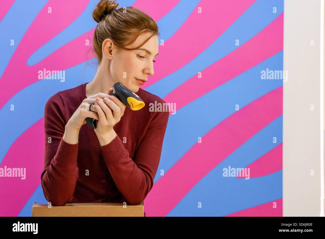 Mitarbeiter, der im Büro auf den umgedrehten Scanner auf dem Paket blickt Stockfoto