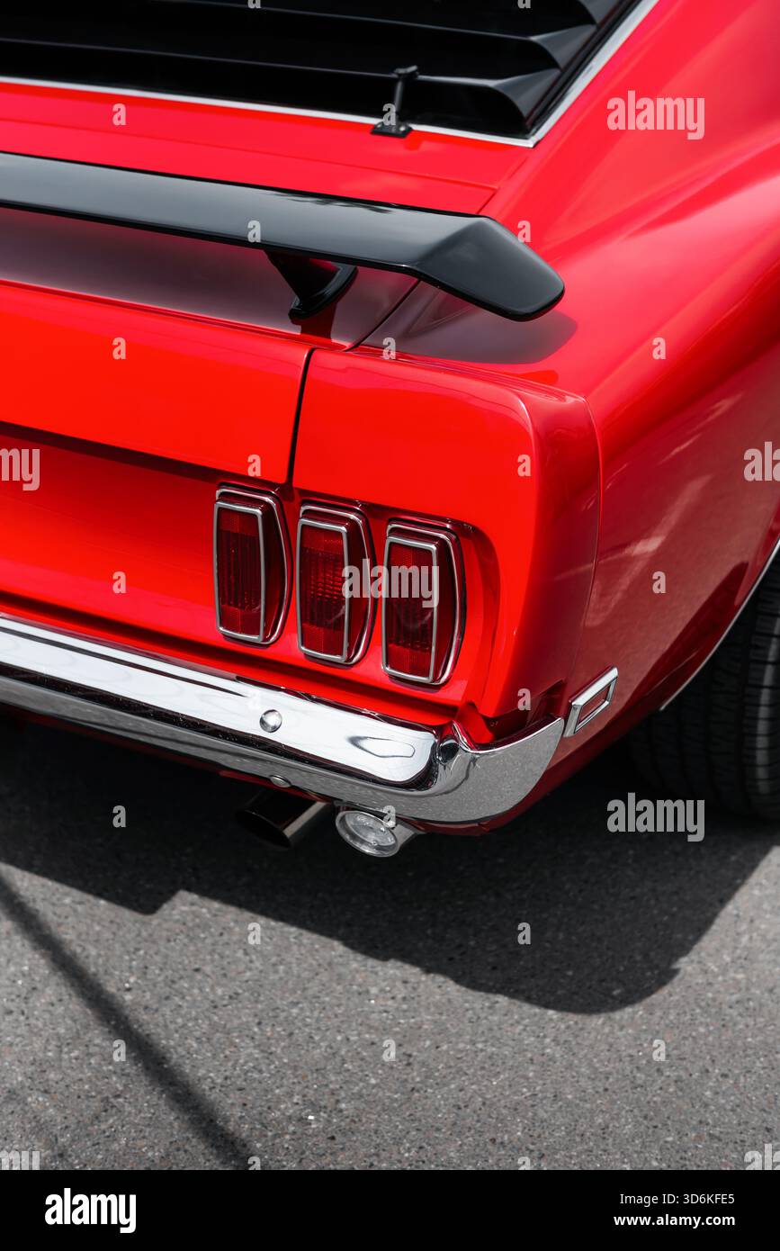 Nahaufnahme des roten Mustang '69: Legendäre dreifache Rückleuchten, verchromter Stoßfänger, schwarzer Heckspoiler. Hintere rechte Ecke des klassischen amerikanischen Muscle Car. Stockfoto