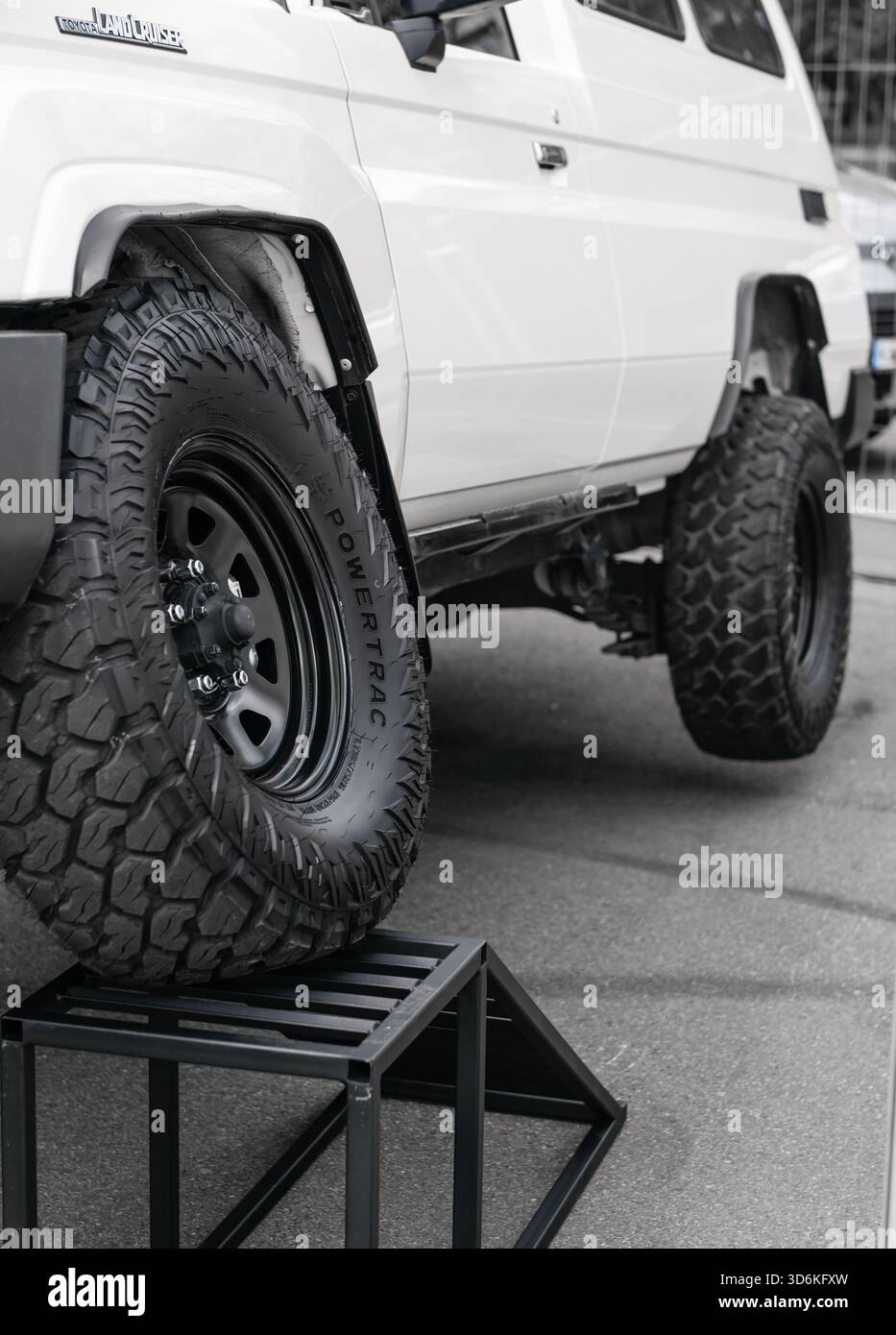 Tiefwinkelansicht eines angehobenen weißen Toyota 4x4 auf einer Rampe, die seine Positionierung unterstreicht. Land Cruiser SUV mit Geländereifen auf schwarzen Felgen. Stockfoto