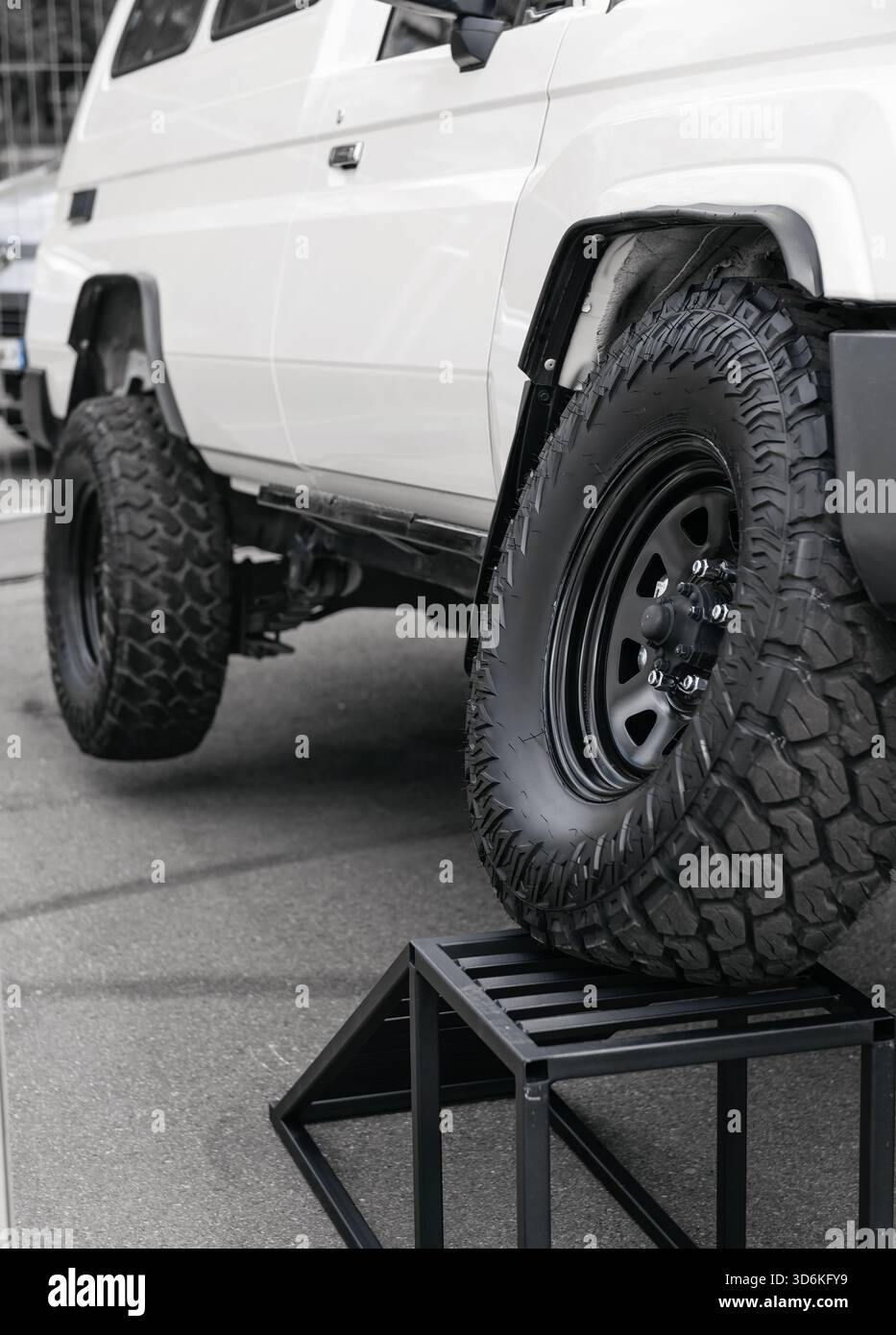 Tiefwinkelansicht eines angehobenen weißen Geländewagens auf einer Displayrampe, die seine Beweglichkeit unterstreicht. Seite des kundenspezifischen 4x4 mit aggressiven Geländereifen Stockfoto