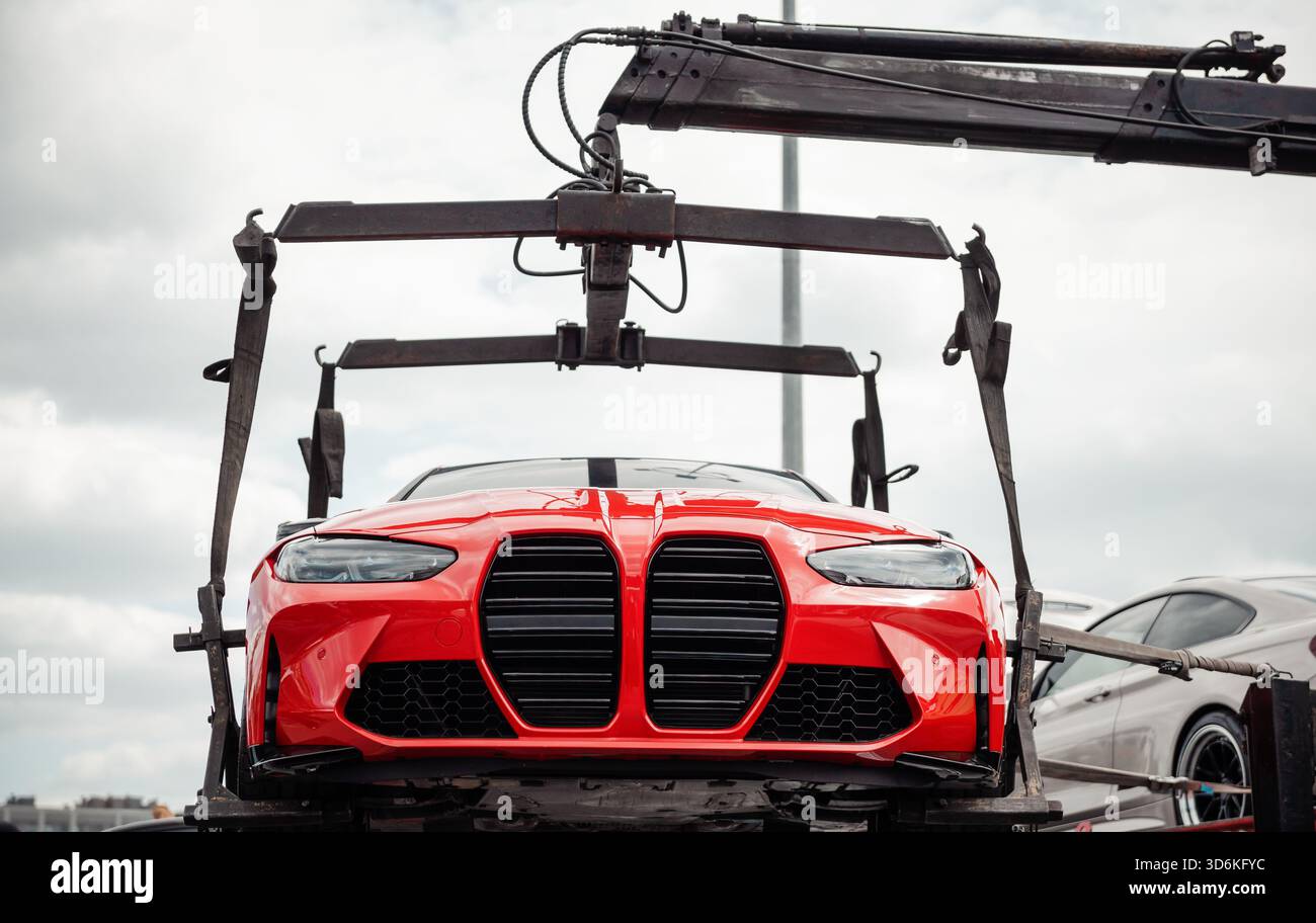 Tiefwinkelansicht des roten Sportwagens, das mit einem Abschleppwagen mit Kran angehoben wird. BMW M3 wird angehoben und abgeschleppt – Parkverstoß oder Mechanikfehler Stockfoto