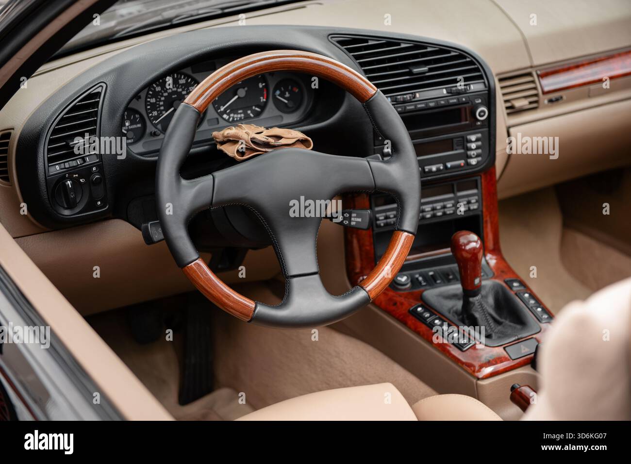 Innenraum aus den 1990er Jahren mit Holzakzenten. Lenkrad und Armaturenbrett eines alten offenen Fahrzeugs. Lederhandschuhe oben auf der Lenksäule. Stockfoto