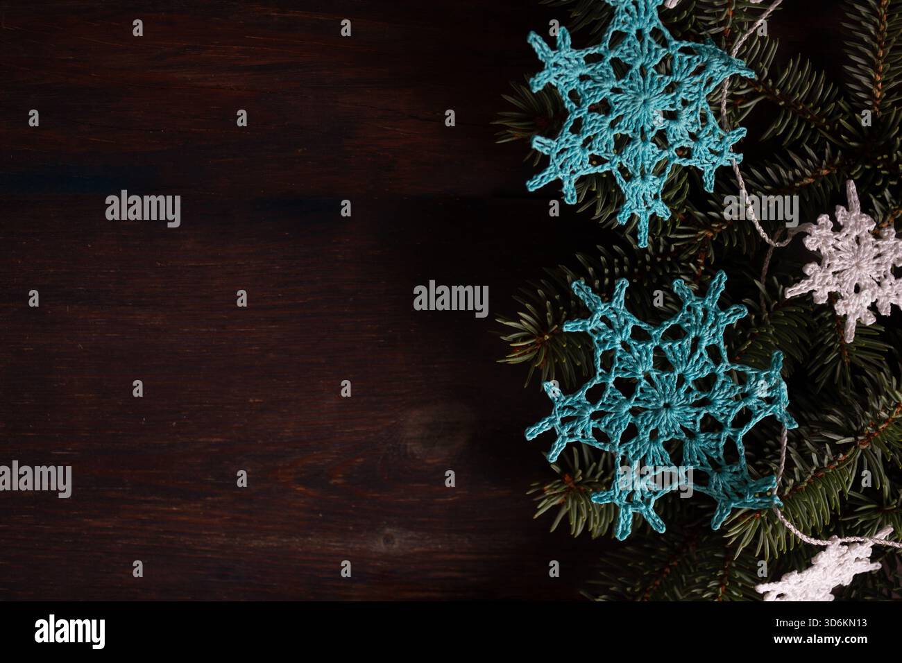 Handgefertigte, gehäkelte Schneeflocken-Ornamente auf dunklem Holzhintergrund mit Tannenzweigen. Weihnachtskomposition mit Platz für Text. Stockfoto