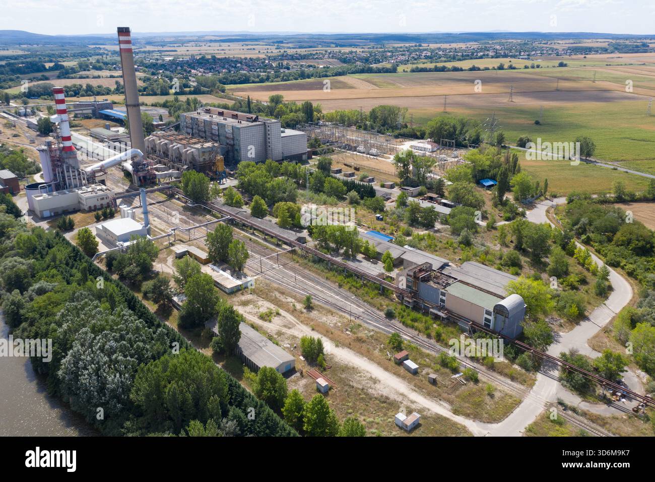 Aus der Vogelperspektive auf ein stillgelegtes Kraftwerk und einen Fabrikkomplex mit Schornsteinen, Bahngleisen und bewachsener Vegetation in einer ländlichen Landschaft Stockfoto