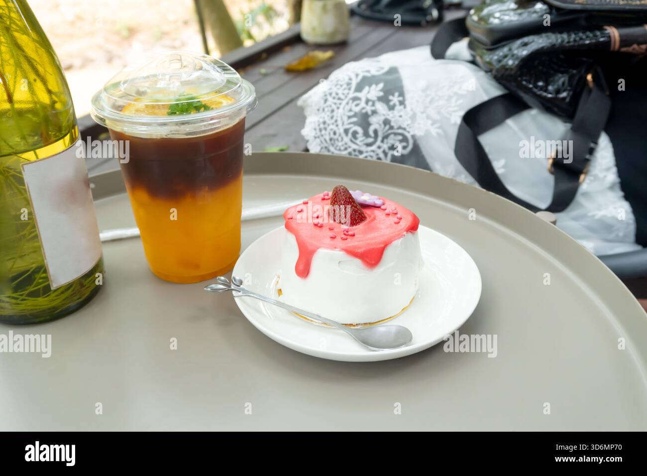 Eiszitronentee in transparentem Kunststoffglas und Erdbeerkuchen mit glasierter Creme auf Mini-weißer Platte mit Mini-Silberlöffel oder Teelöffel werden serviert Stockfoto