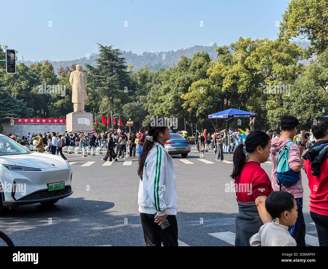 Mao Zedong Statue, Changsha, China. Geschäftige Straßenszene in der Nähe der Hunan University mit Fußgängern, Autos und üppigen Bäumen unter klarem Himmel. Stockfoto