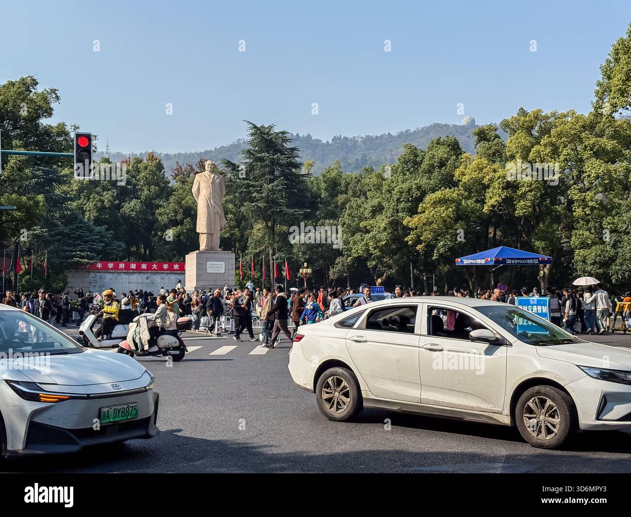 Mao Zedong Statue am Eingang der Hunan Universität in Changsha, China, inmitten einer überfüllten Straße voller Autos, Motorroller und Fußgänger Stockfoto