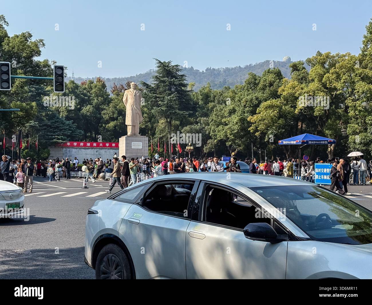 Eine geschäftige Stadtstraße in der Nähe der Hunan University in Changsha, China, mit einer prominenten Statue, zahlreichen Fußgängern und Autos, die das tägliche Leben der Stadt darstellen Stockfoto