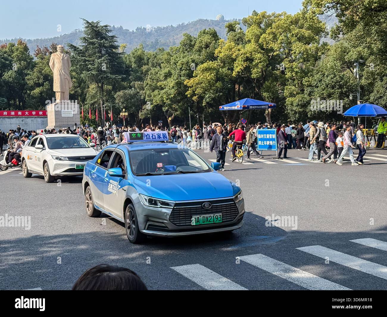 Eine überfüllte Straße voller Autos und Fußgänger in der Nähe der Hunan University in Changsha, China. Mit einer Statue von Mao Zedong und geschäftigen urbanen Aktivitäten. Stockfoto