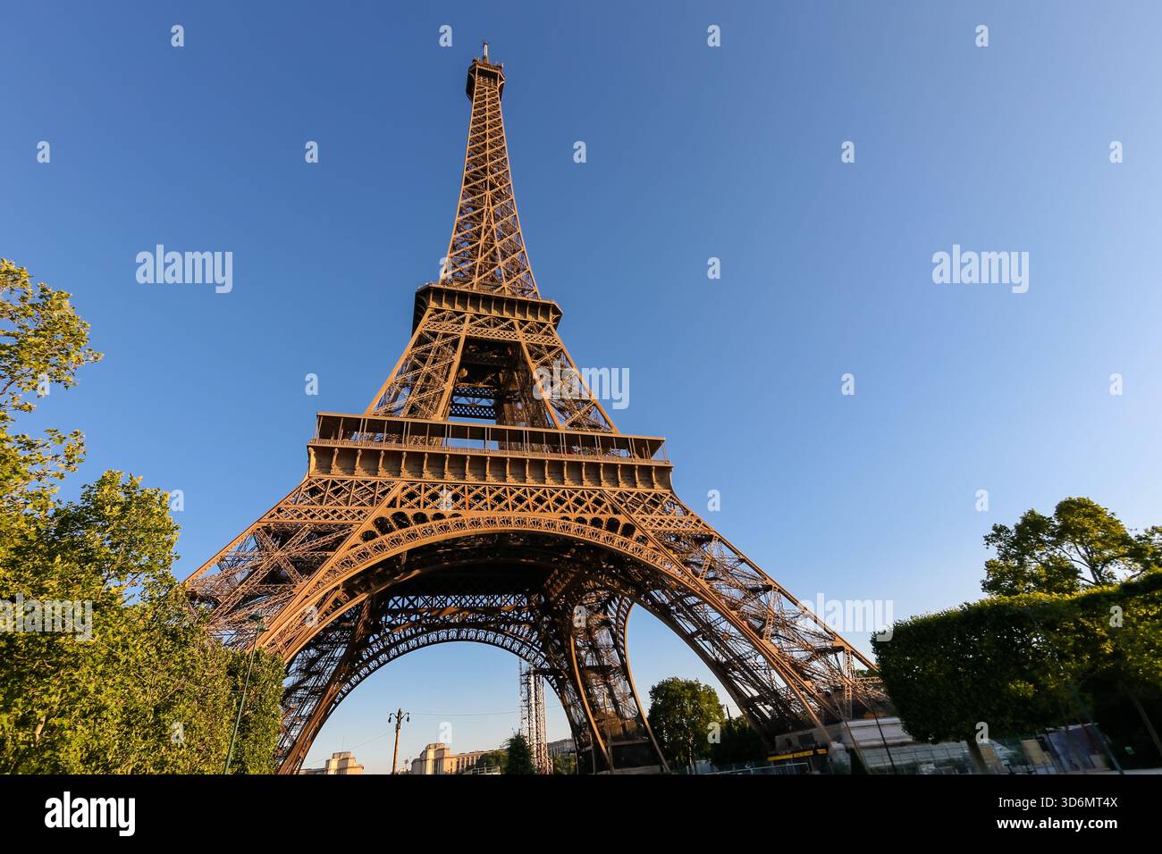 Nahaufnahme der eisernen Gitterstruktur des Eiffelturms mit warmem Morgenlicht vor einem klaren blauen Himmel in Paris, Frankreich. Stockfoto