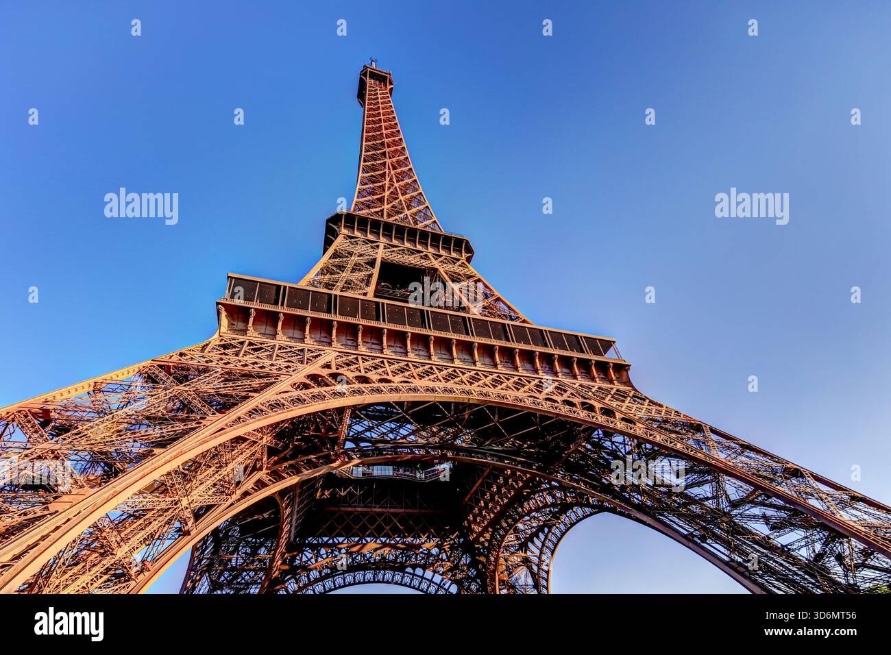 Nahaufnahme der eisernen Gitterstruktur des Eiffelturms mit warmem Morgenlicht vor einem klaren blauen Himmel in Paris, Frankreich. Stockfoto
