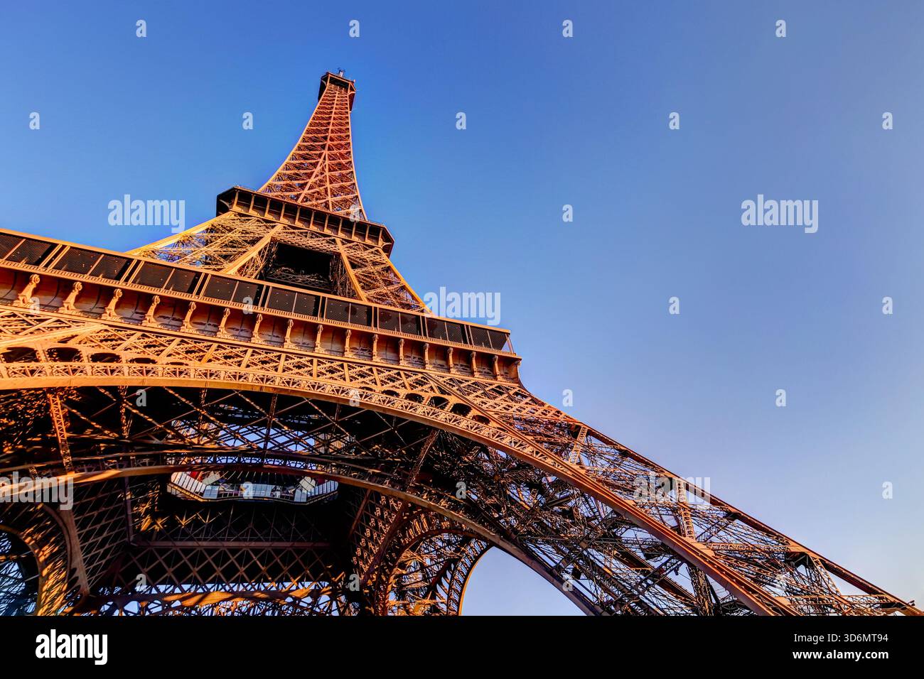 Nahaufnahme der eisernen Gitterstruktur des Eiffelturms mit warmem Morgenlicht vor einem klaren blauen Himmel in Paris, Frankreich. Stockfoto
