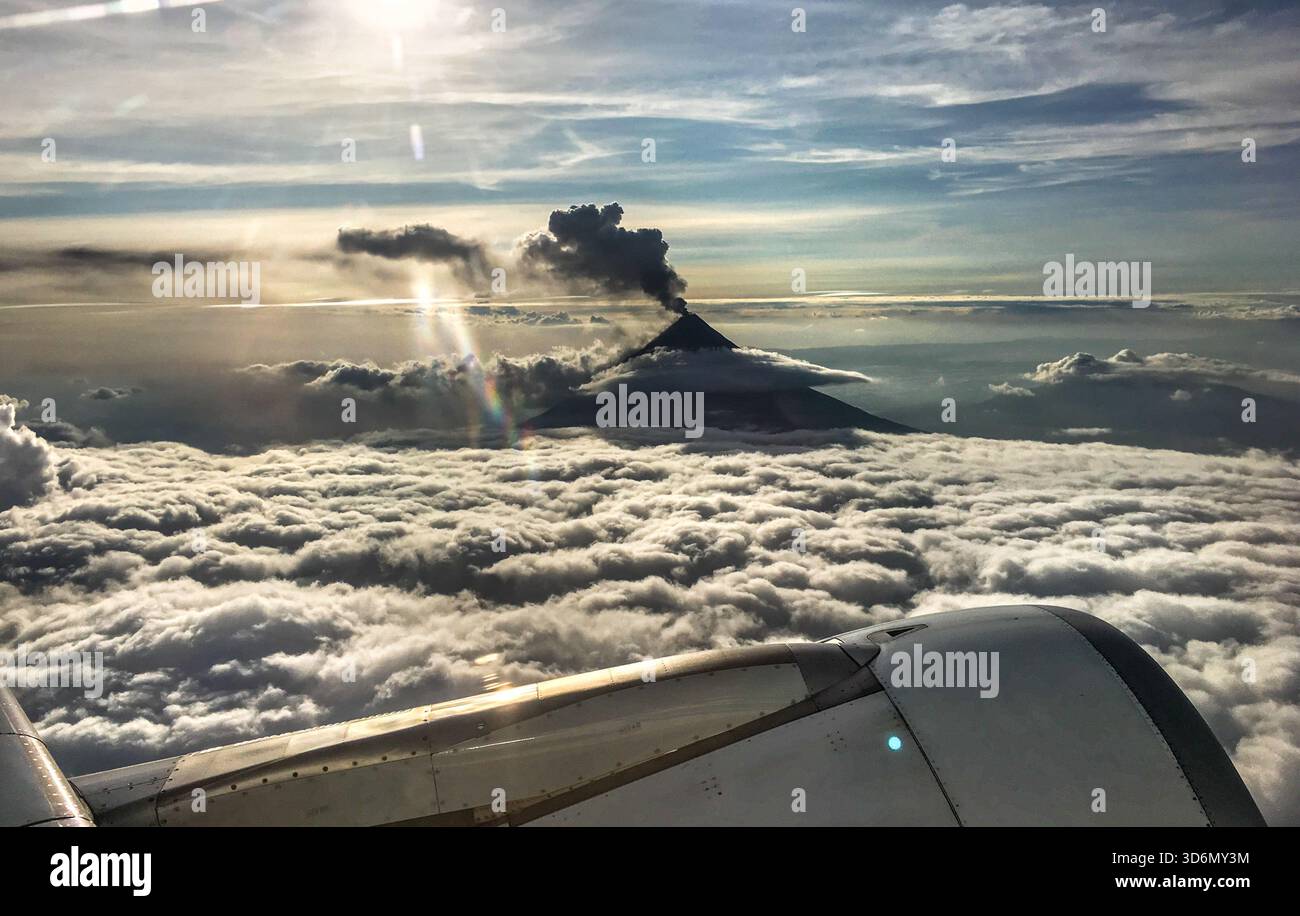 Aus der Vogelperspektive eines Cebu Pacific Flugzeugfensters auf den Vulkan Mayon, der über dem Gipfel aufragt und durch Wolkenschicht auftaucht - Smartphone-aufgenommenes Stockfoto