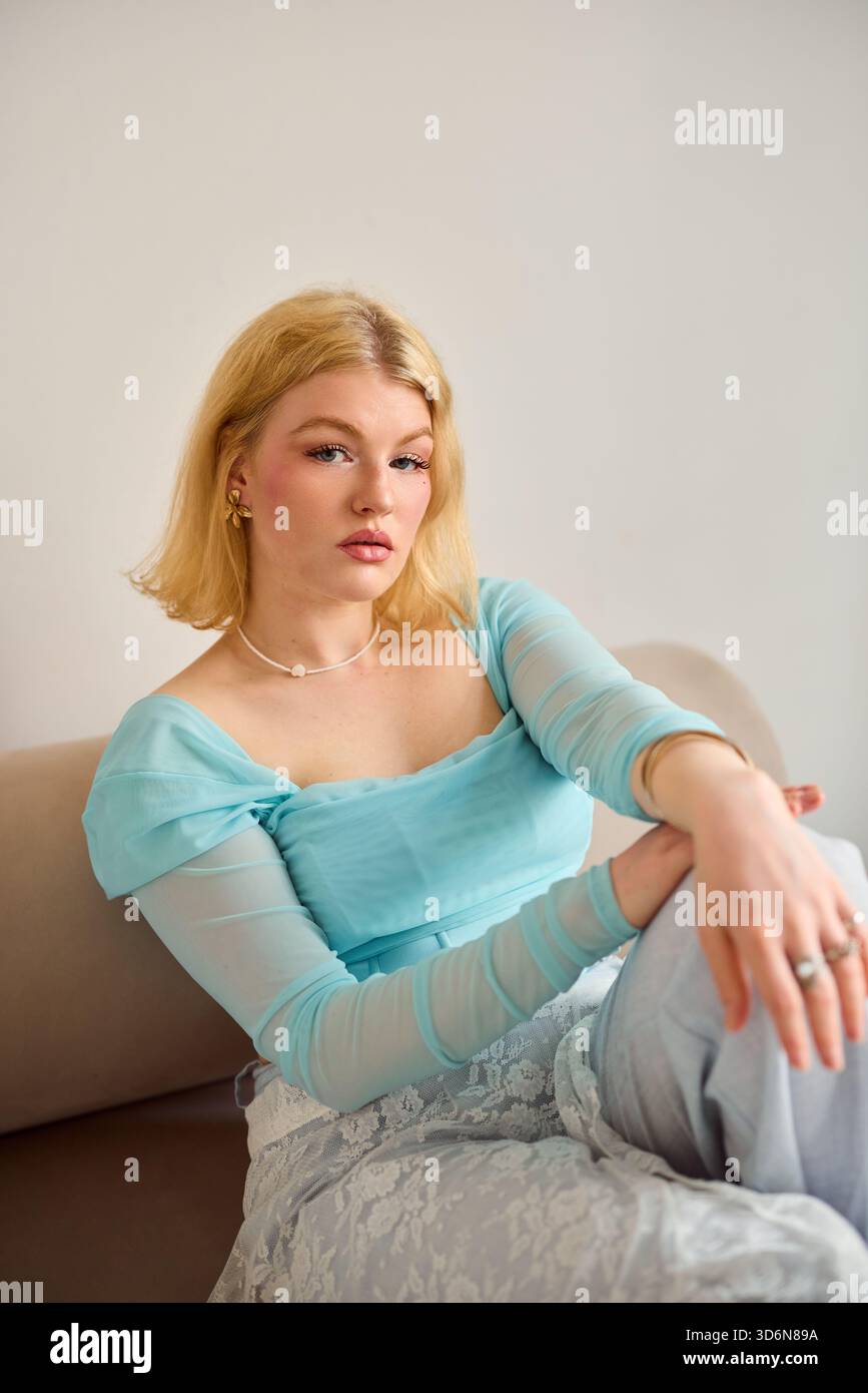 Junge Frau in hellblauem Oberteil, die sich auf einem beigen Sofa entspannt Stockfoto