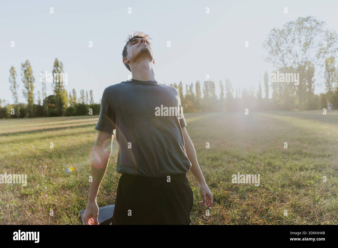 Junger Mann, der tief draußen im Herbstfeld atmet. Er steht auf einem Feld Stockfoto