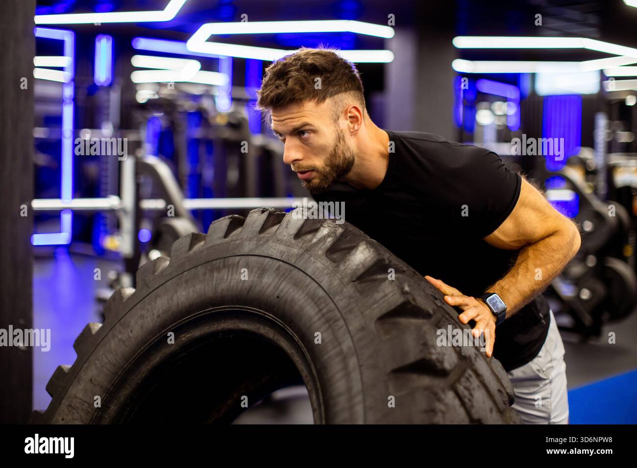 Ein muskulöser Mann trainiert intensiv in einem modernen Fitnessstudio, dreht einen großen Reifen und zeigt Hingabe und Kraft. Stockfoto