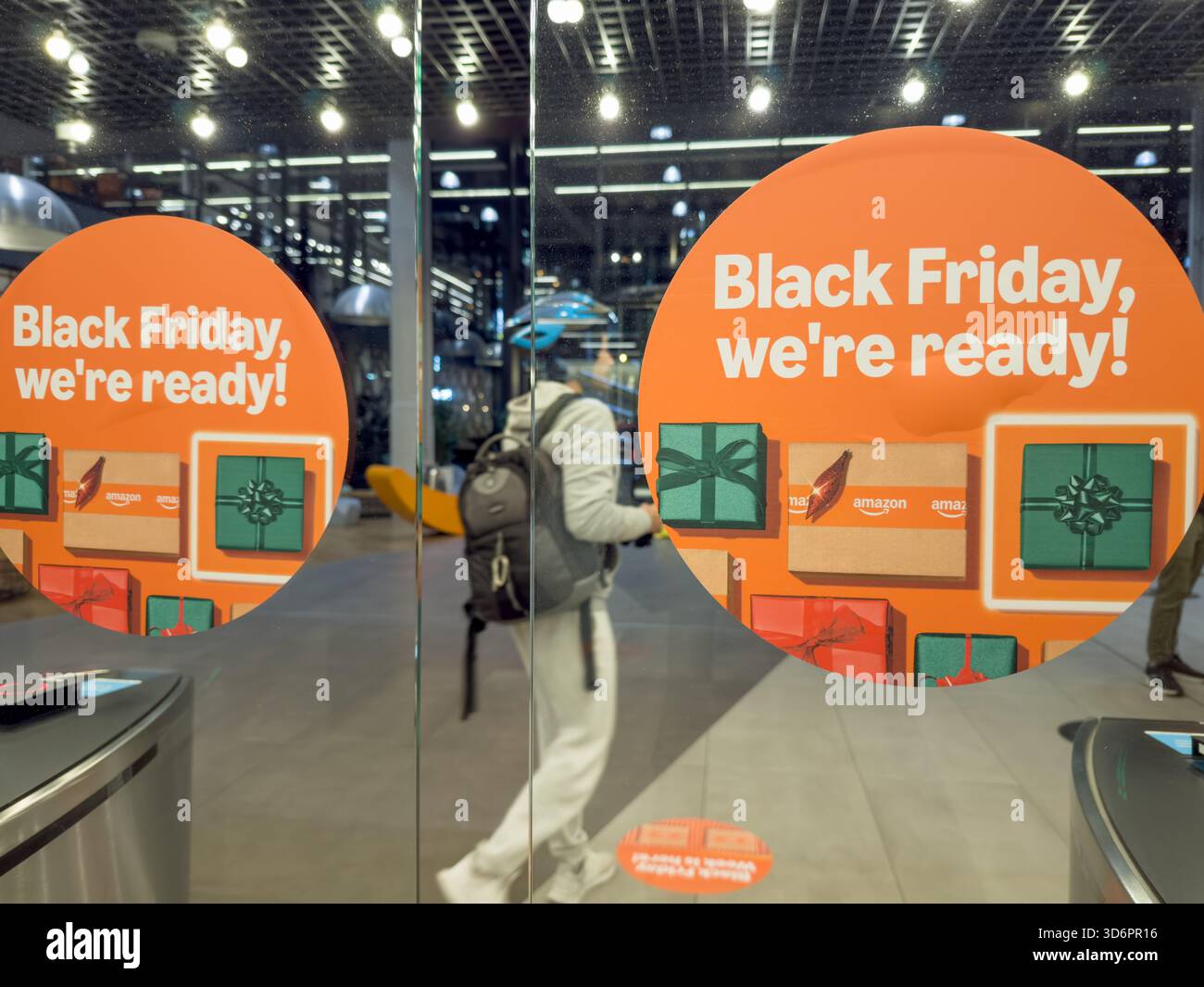 Ein Käufer geht durch eine Schiebetür, die mit Amazon Black Friday Week-Verkaufspostern verziert ist und die saisonalen Einzelhandelsaktionen in einem Londoner Geschäft beleuchtet Stockfoto