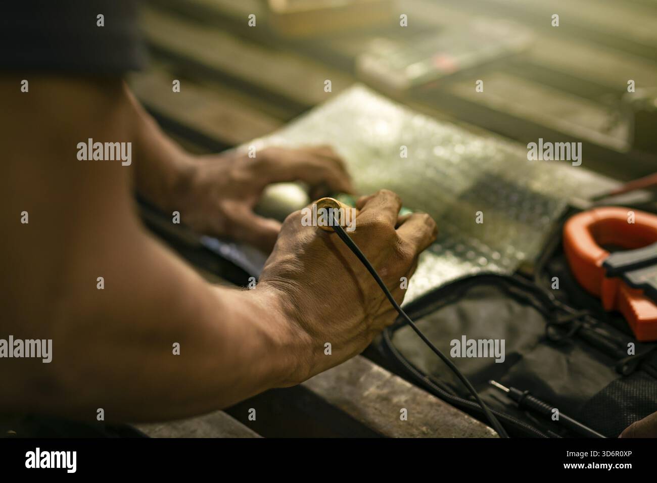 Nahaufnahme eines Mannes, der einen Lötkolben auf einer elektronischen Leiterplatte auf einem Tisch benutzt Stockfoto