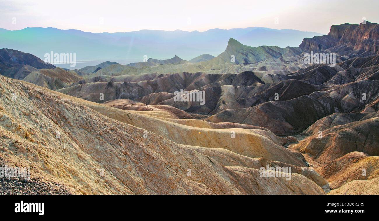 Ausgedehnte Badlands-Landschaft im Death Valley mit erodierten Hügeln, Graten und überlagerten Felsformationen unter einem hellen, trüben Himmel bei Sonnenaufgang. Stockfoto