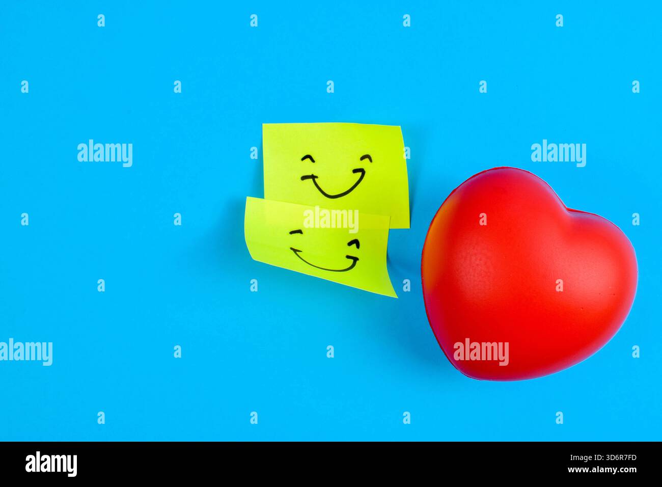 Rotes Herz und zwei Smiley-Haftnotizen auf blauem Hintergrund, die Liebe, Glück und emotionale Verbindung durch lebendigen Kontrast symbolisieren. Stockfoto