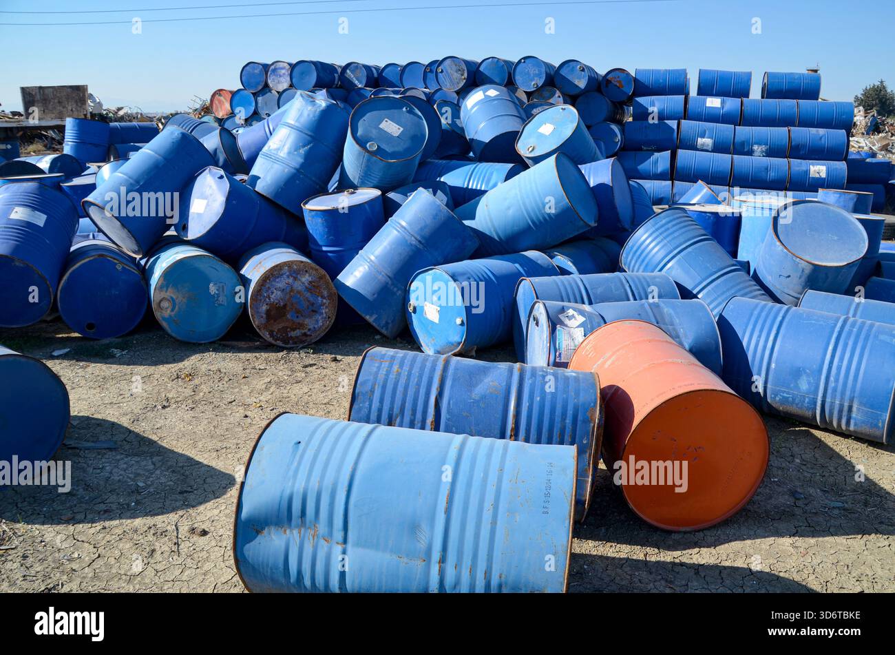 Ein riesiger Haufen blauer und oranger Metallfässer und Abfallfässer auf einem industriellen Schrottplatz oder einem Lagerplatz für Gefahrstoffe unter blauem Himmel. Stockfoto