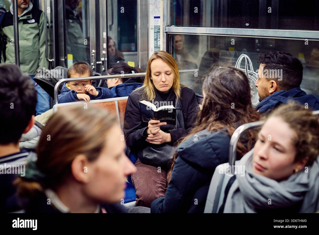 Paris, Frankreich - März 2025: Eine Frau wird in ein Buch aufgenommen, während sie im 15. Pariser Arrondissement mit der U-Bahn fährt. Stockfoto