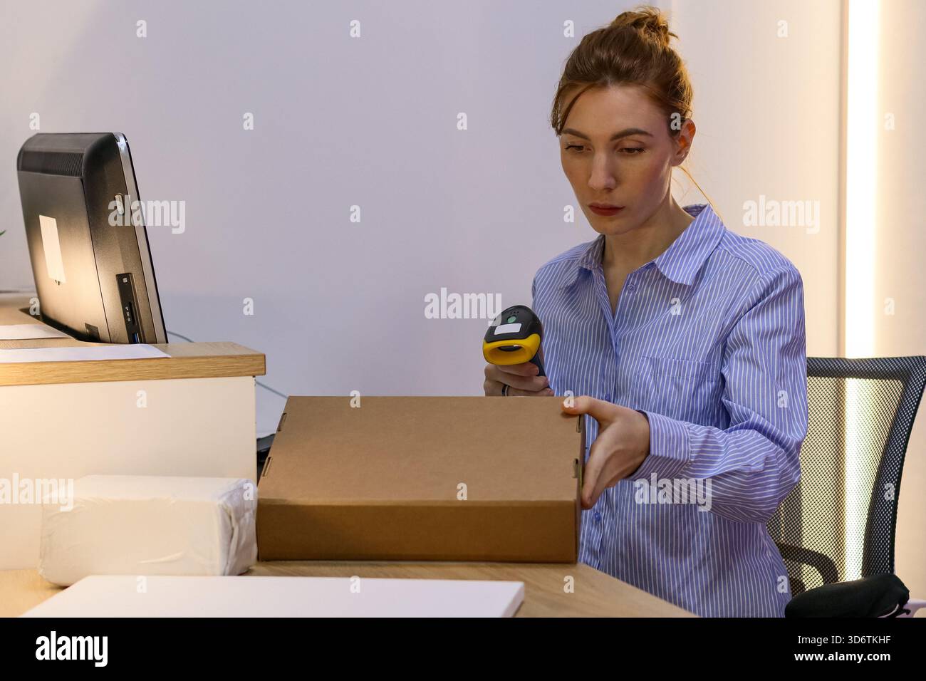 Weibliche Mitarbeiter scannen Barcode auf Papppaketen mit Handgerät an einem Arbeitsplatz mit Bildschirm. Stockfoto