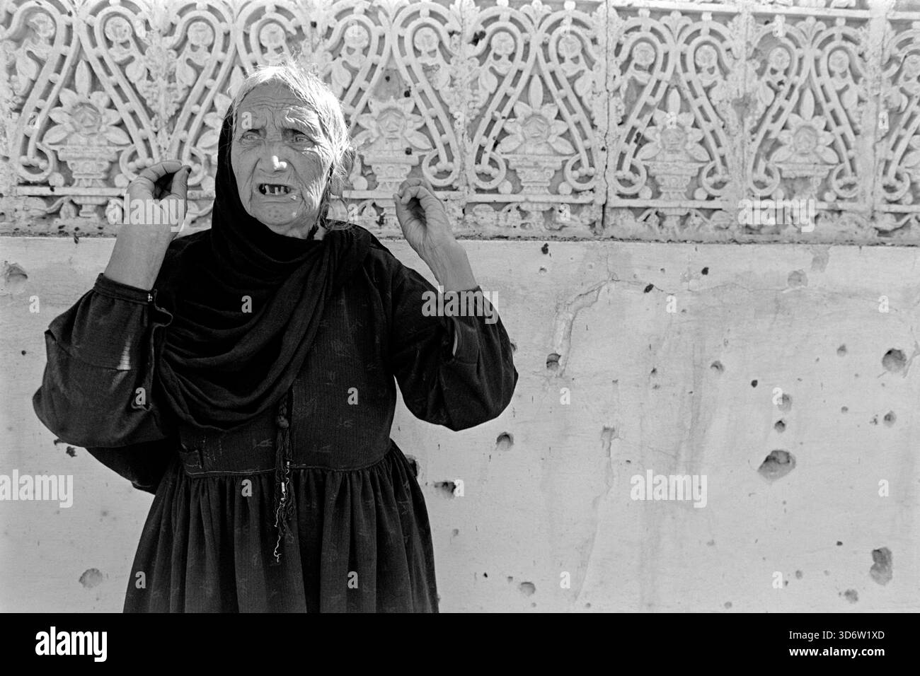 Eine ältere afghanische Frau, die vor einer mit Splittern markierten Wandtasche steht, reagiert, nachdem am 18. April 1988 in Kabul, Afghanistan, eine Rakete ihr Haus getroffen hat, bei der mehrere Kinder verletzt werden, die in einem Wohnviertel spielen. Raketen, die von den Mudschaheddin-Guerillakämpfern abgefeuert wurden, werden von den umliegenden Hügeln in die Stadt geschossen, um die Bevölkerung zu terrorisieren und die Regierung zu schikanieren. Stockfoto