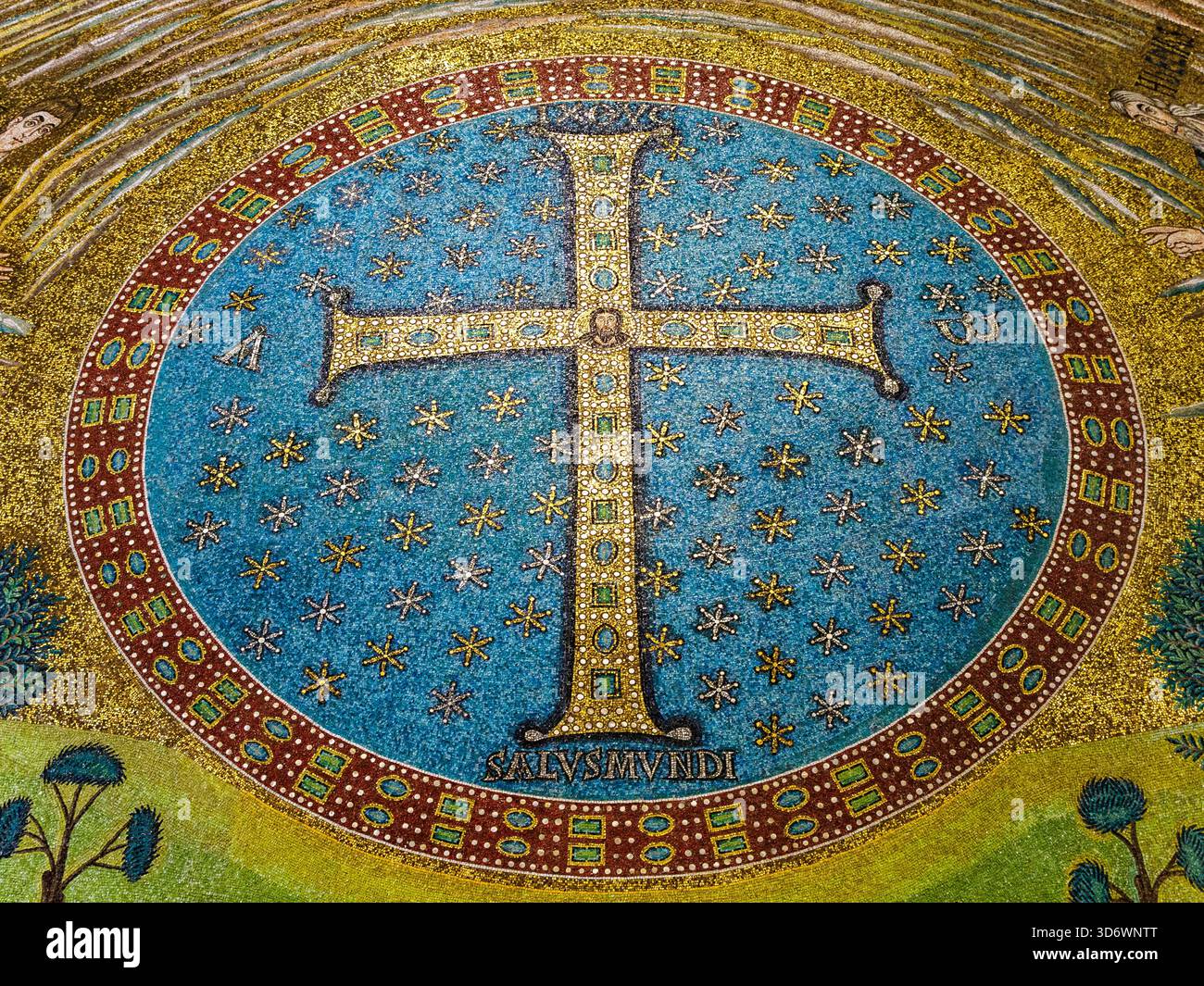 Detail des Apsienmosaiks. Innerhalb einer Scheibe mit einem violetten Rahmen, der mit Edelsteinen besetzt ist, auf einem blauen Hintergrund mit 99 goldenen Sternen, befindet sich ein mit Juwelen besetztes Kreuz. An der Kreuzung der beiden Arme des Kreuzes ist das Gesicht Christi dargestellt. An den Seiten der kürzeren Arme des Kreuzes befinden sich die Buchstaben Alpha und Omega, die an das zweite Kommen Christi erinnern, während am Fuße des Kreuzes „Salus Mundi“ steht, was auf die Rolle des Erlösers anspielt – Basilica di Sant'Apollinare in Classe-Ravenna, Italien Stockfoto