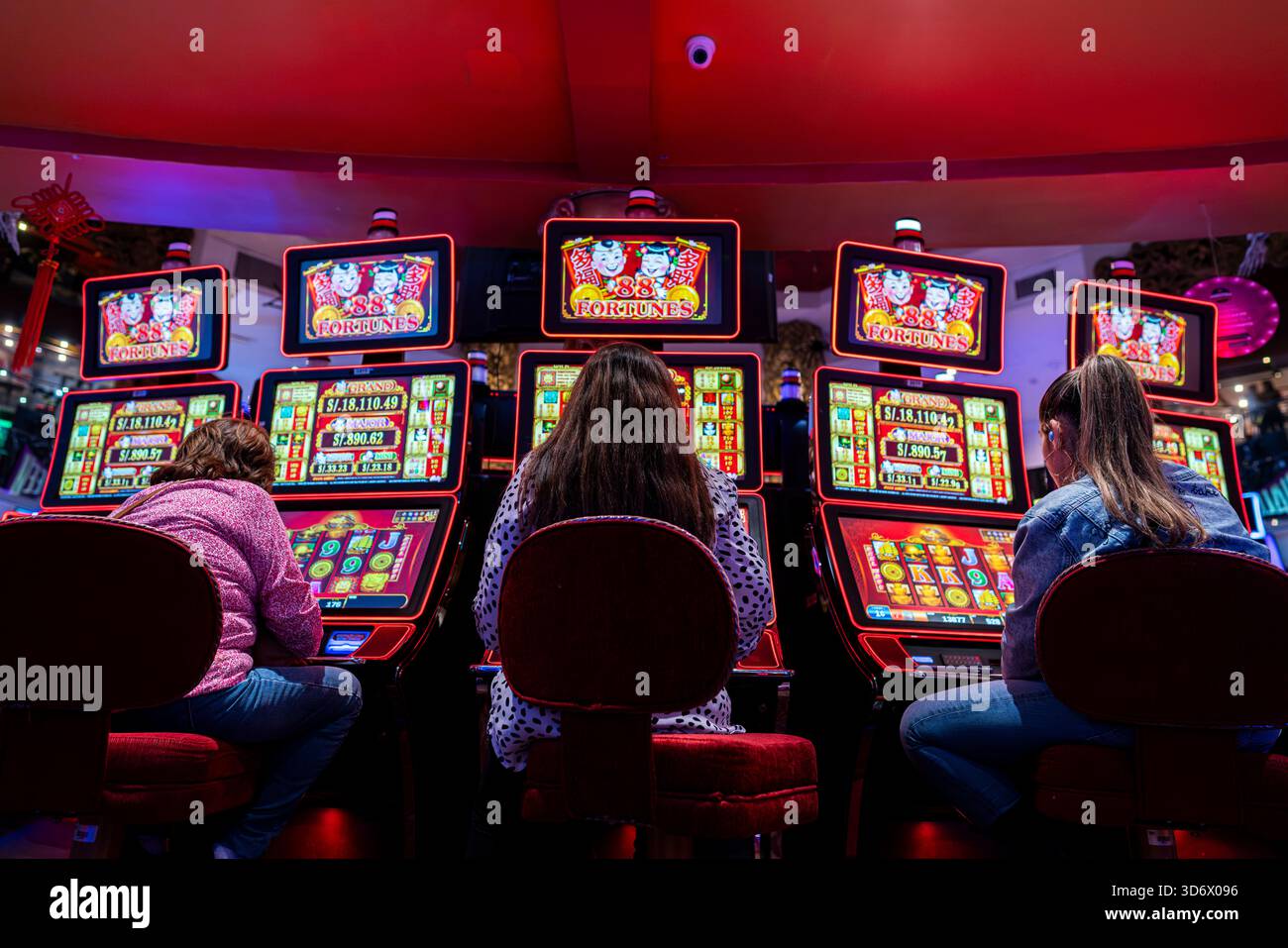 Frauen spielen beleuchtete 88 Fortune Spielautomaten in einem lebhaften Casino mit hellen Bildschirmen und bunten Spiellichtern. Stockfoto