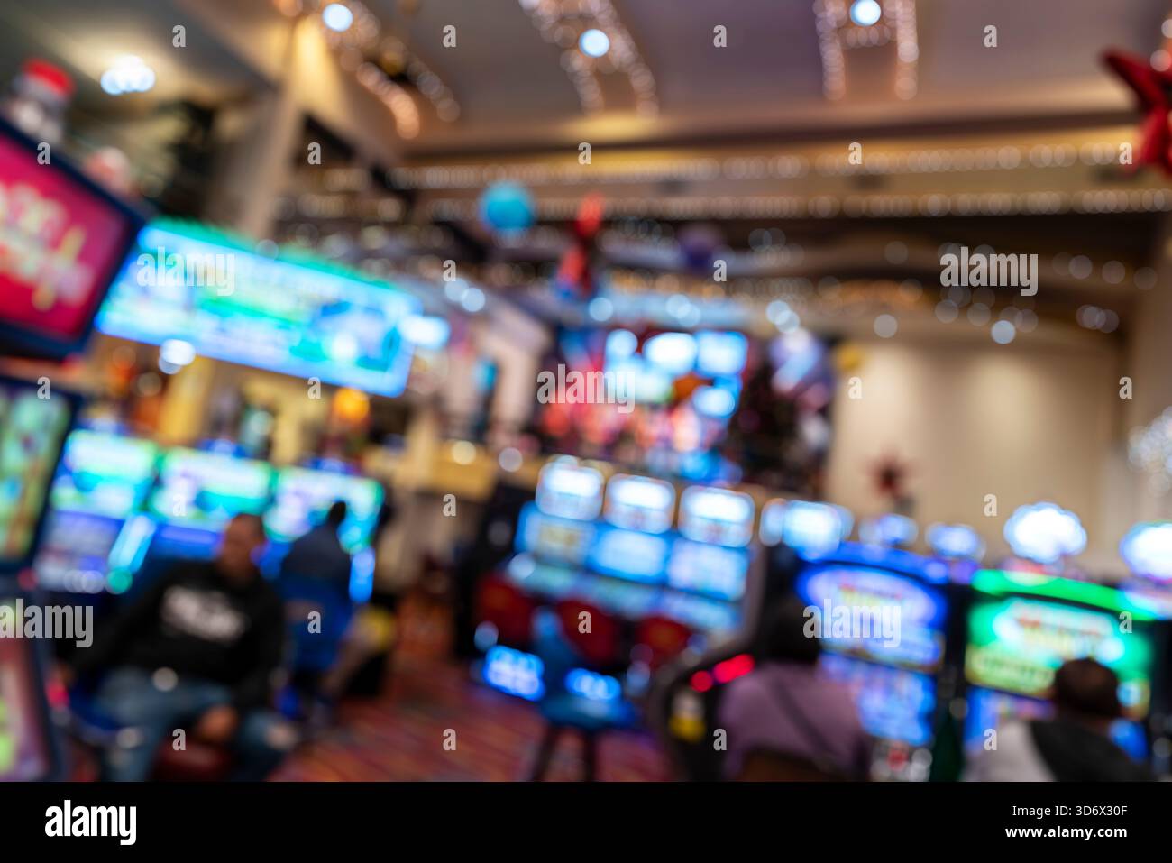 Verschwommenes Casino-Interieur mit hellen Spielautomaten, farbenfroher Beleuchtung und Menschen, die eine abstrakte Unterhaltungsatmosphäre bilden. Stockfoto