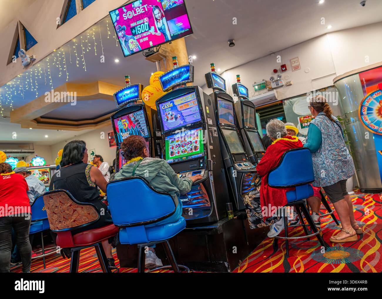Menschen spielen Spielautomaten in einem lebhaften Casino mit hellen Bildschirmen, bunten Lichtern, festlicher Dekoration und einer aktiven Spielumgebung. Stockfoto