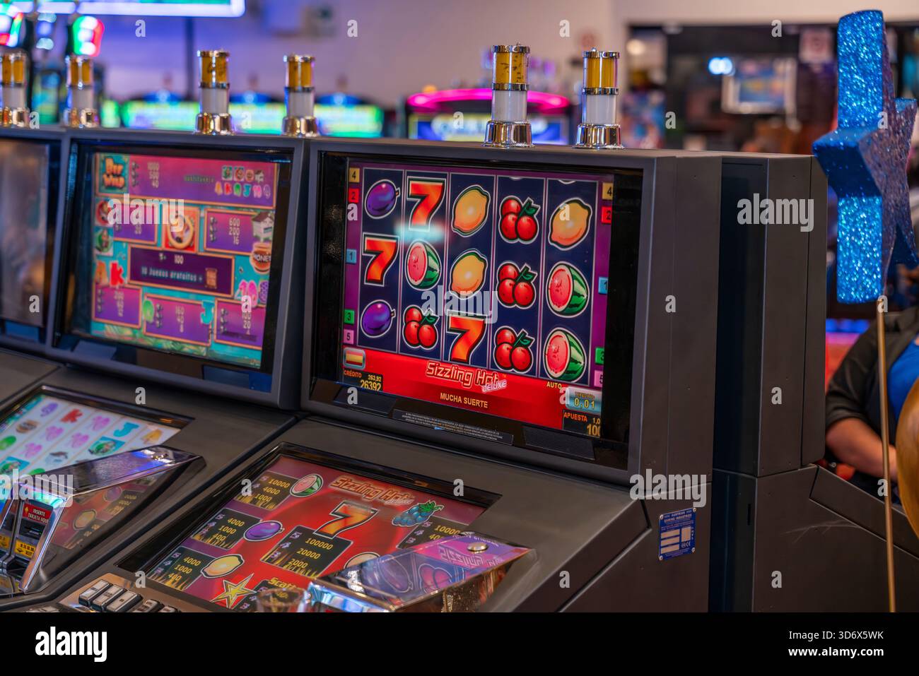 Farbenfroher Spielautomat mit Fruchtsymbolen und Sieben in einer lebhaften Casino-Umgebung, die Spielbildschirme und helle Grafiken hervorhebt. Stockfoto