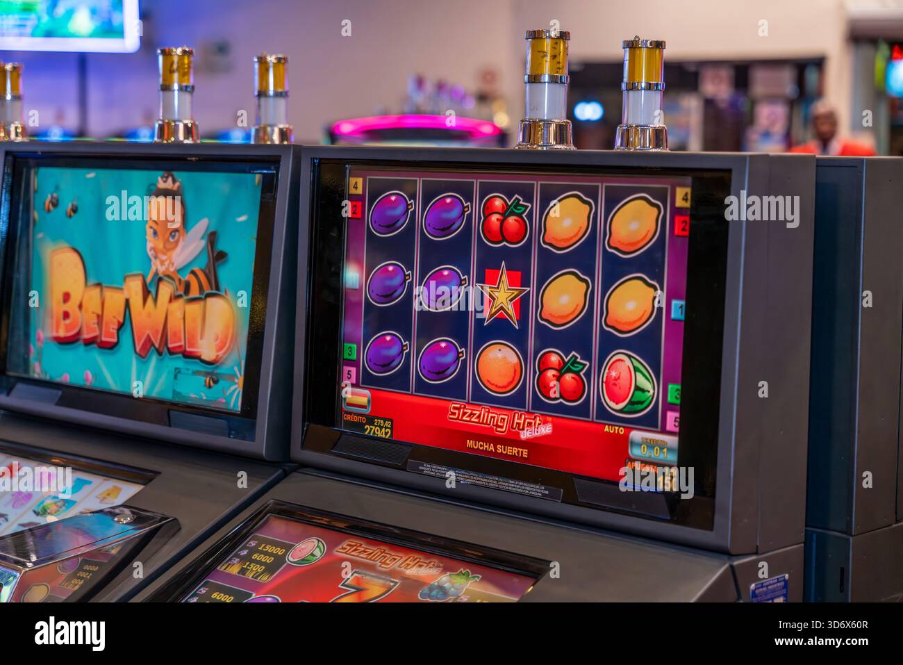 Farbenfroher Spielautomat mit Fruchtsymbolen, Sternen und Sieben in einer lebhaften Casino-Umgebung mit verschwommenen Menschen im Hintergrund. Stockfoto