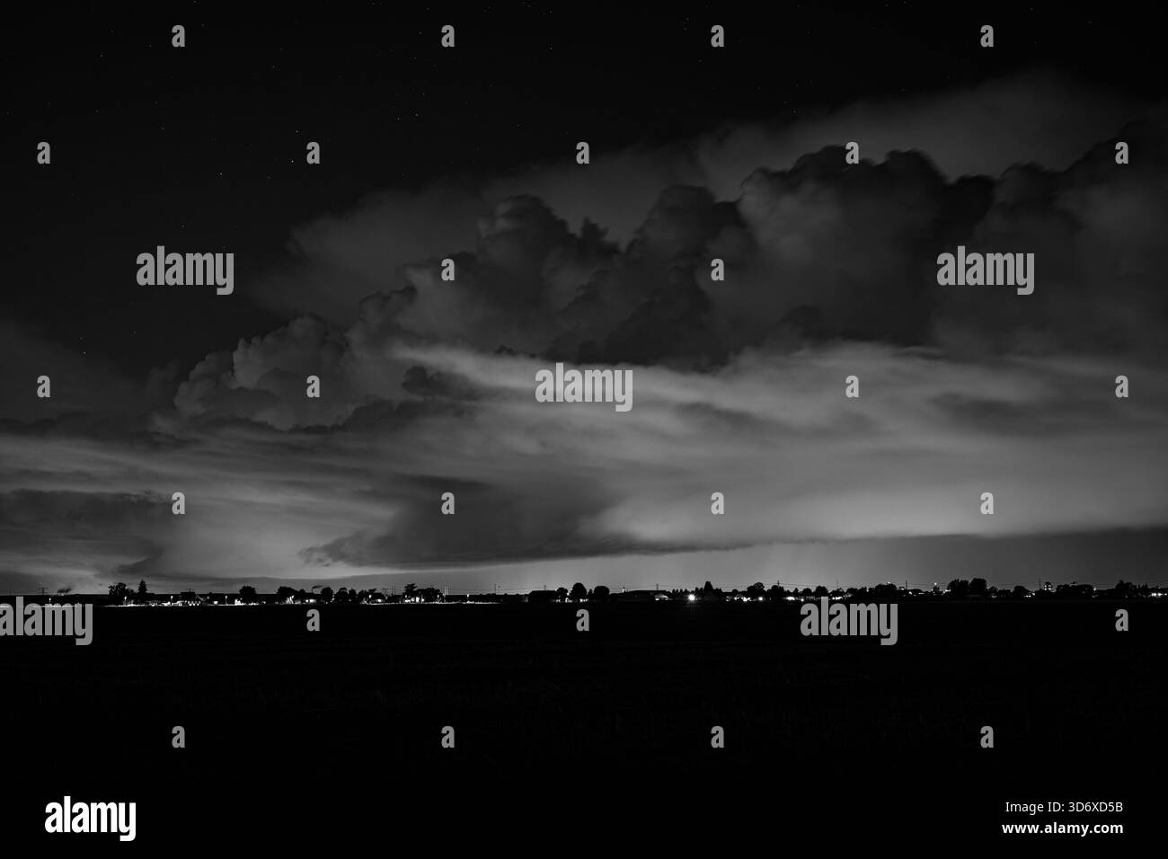 Kräftiges, nächtliches Gewitter in Schwarzweiß mit Blitzen über einem weit entfernten, glühenden Horizont der Stadt Stockfoto