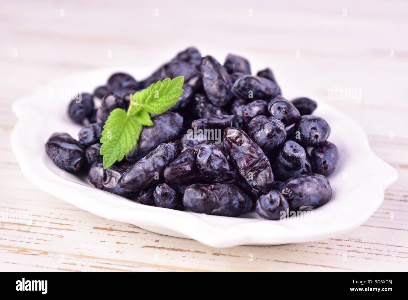 Geißblatt-Beeren auf einem Teller auf weißem hölzernem Hintergrund. Nahaufnahme. Stockfoto