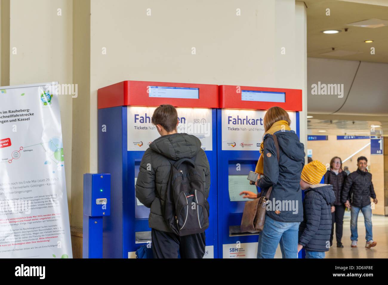 Passagiere am Hannover Hauptbahnhof nutzen Fahrkartenautomaten unter den großen Abfahrtstafeln. Stockfoto