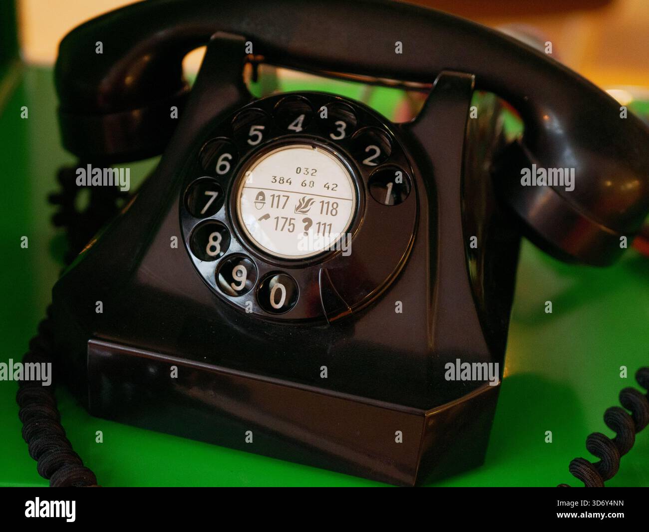Ein Vintage-schwarzes Drehwahltelefon auf grüner Oberfläche. Das Gerät repräsentiert frühe Kommunikationstechnologie und klassisches Industriedesign Stockfoto