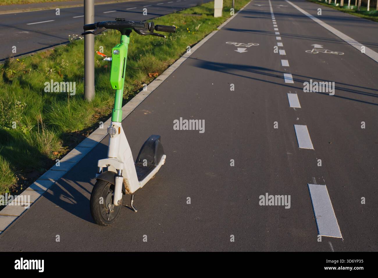 Ein leuchtend grüner Elektroroller steht auf einer Radstrecke in Neuss, Deutschland. Der Weg ist gut gepflegt, von Gras umgeben, und es ist ein sonniges Achterfeld Stockfoto