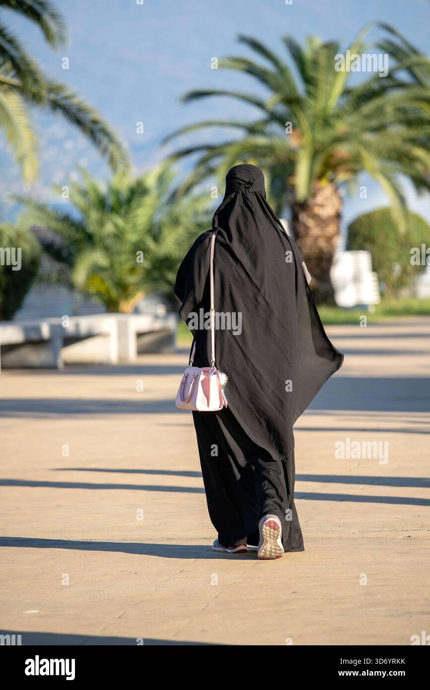 Arabisches muslimisches Mädchen in schwarzem Gewand auf der Straße. Silhouette einer arabischen Frau in traditionellem muslimischen schwarzen Hijab oder Jilbab. Rückansicht. Stockfoto
