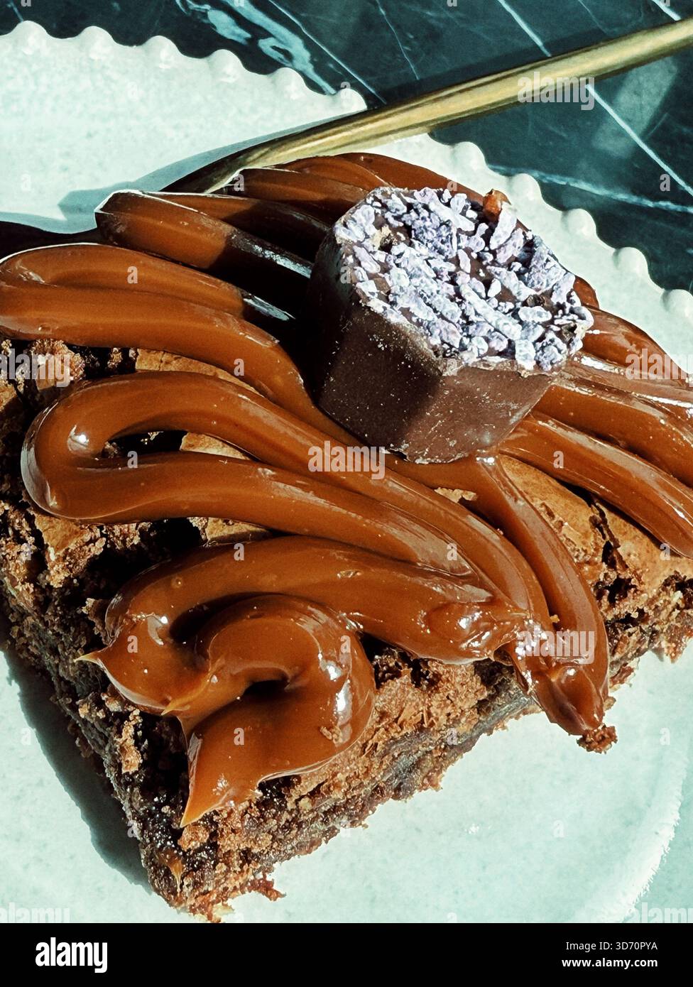 Nahaufnahme eines reichhaltigen Schokoladen-Brownie, gekrönt mit Schoko-Zuckerguss und einem dekorativen Schokoladen-Trüffel auf einem weißen Teller Stockfoto