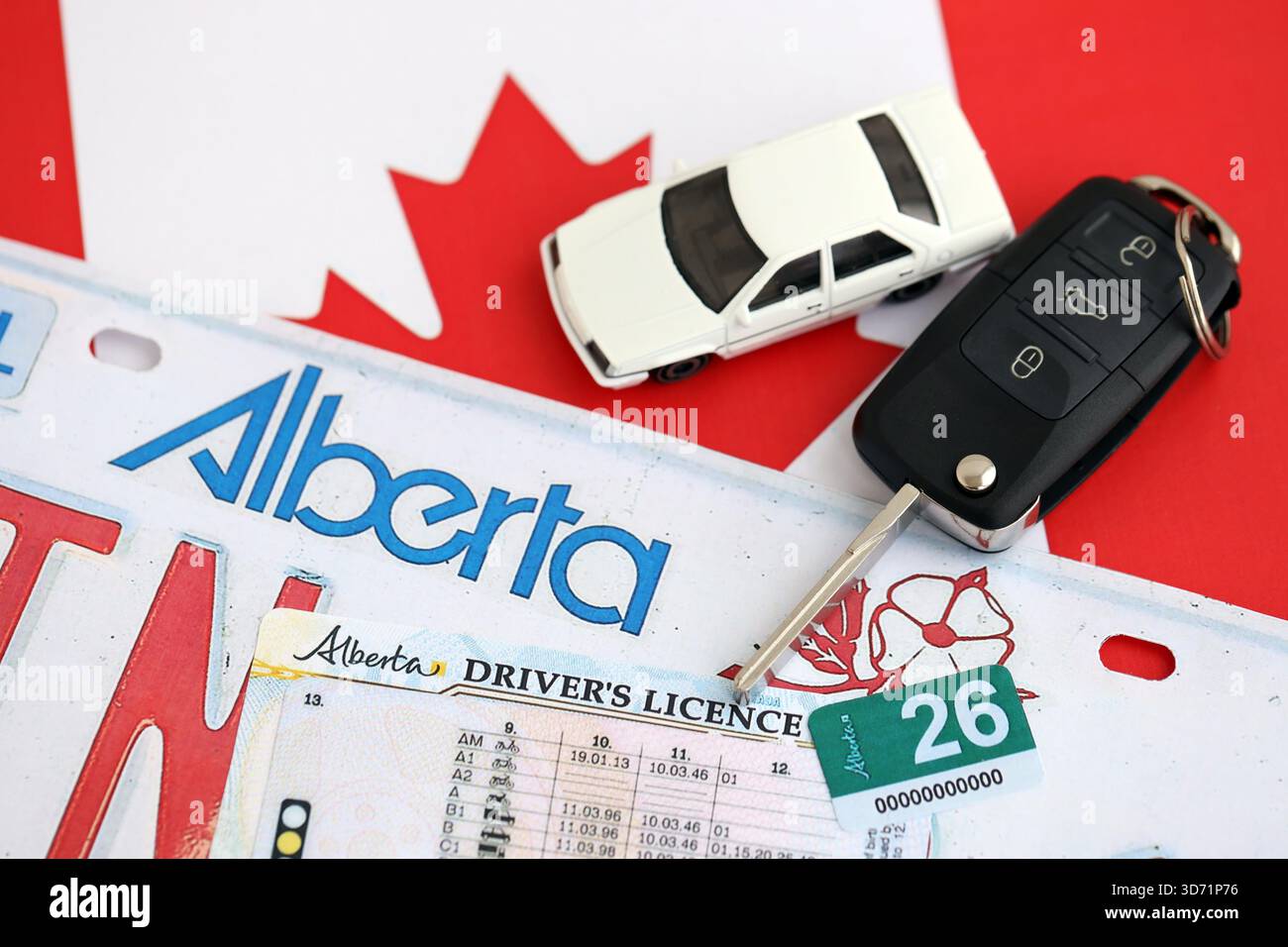 Alberta canadian Autokennzeichen und Zündschlüssel auf der Flagge von Kanada Nahaufnahme. Führerschein- und Zulassungskonzept Stockfoto