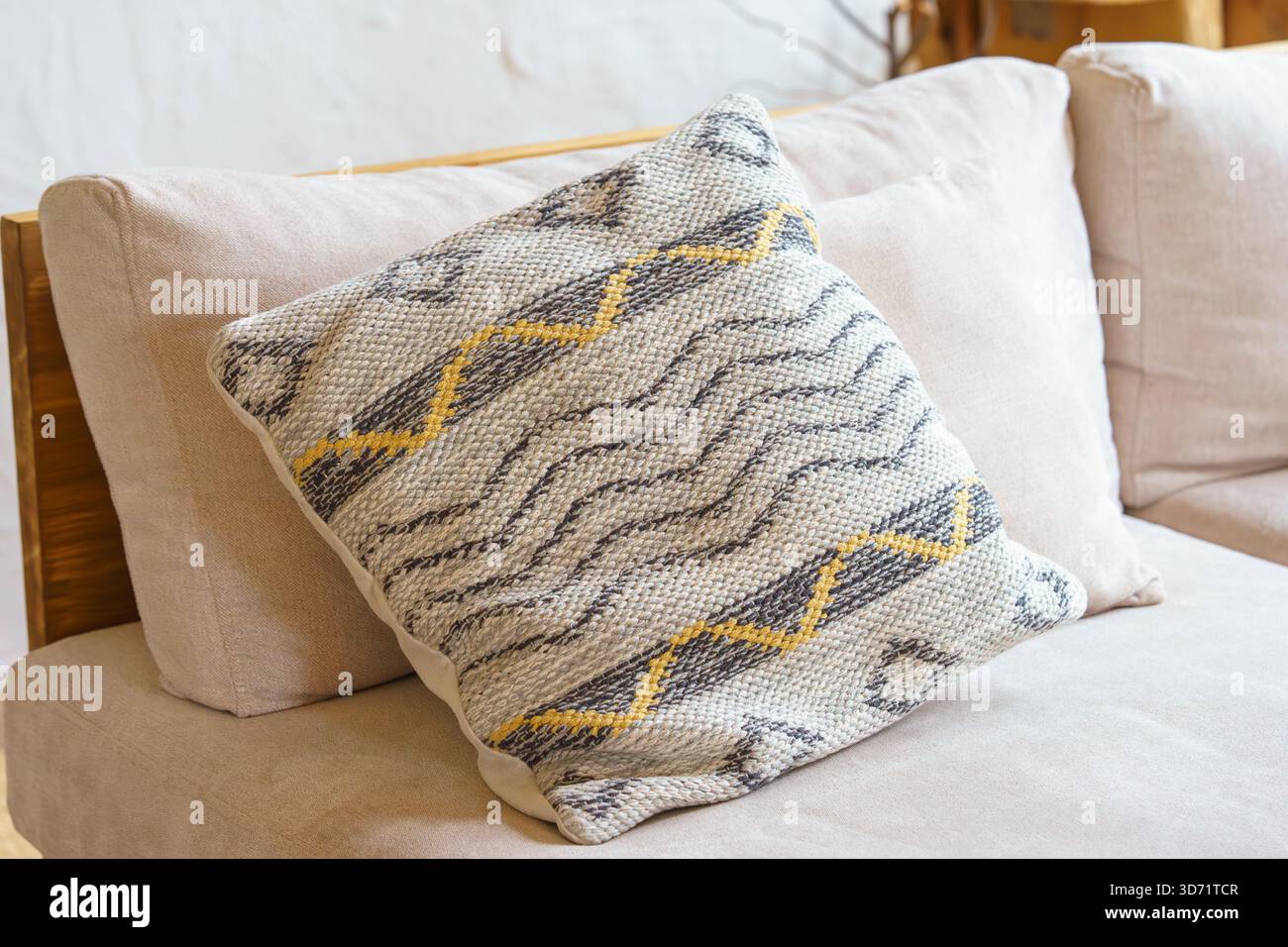Weiches Dekokissen, Kissen mit geometrischer Webstruktur und gelbem Zickzackmuster auf hellbeigem Sofa. Gemütliches, minimalistisches skandinavisches Interieur mit Stockfoto