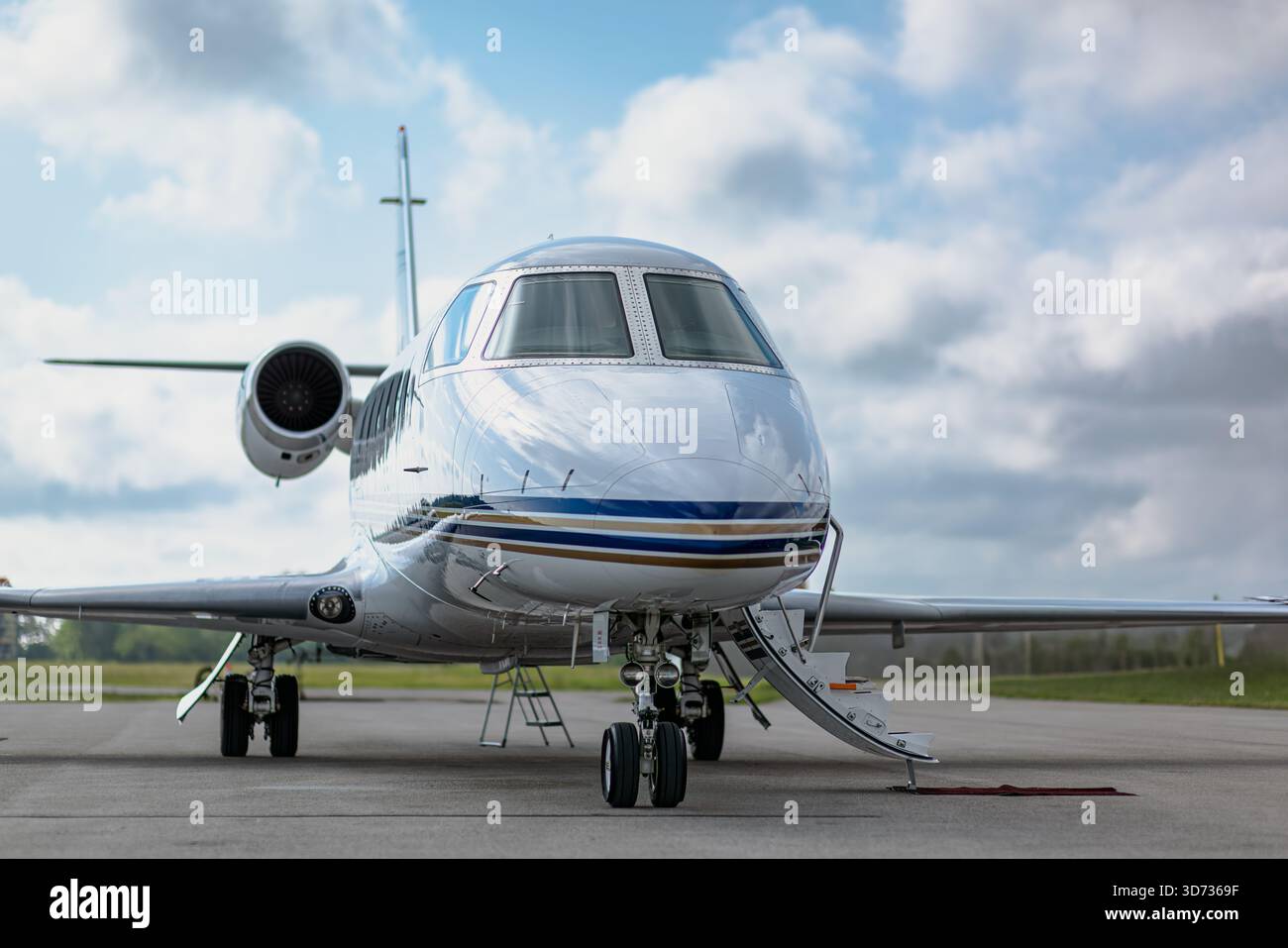 Vorderansicht von drei Vierteln auf den weißen Geschäftsjet mit verlängerter Eingangstreppe. Bewölkter blauer Himmel im Hintergrund. Stockfoto
