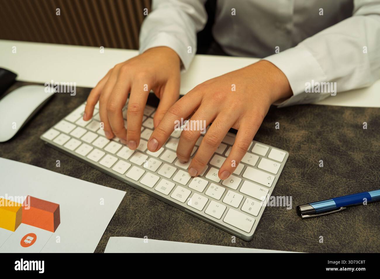 Die Hände einer Person, die auf einer Computertastatur mit Geschäftsdokumenten auf einem Schreibtisch schreibt Stockfoto