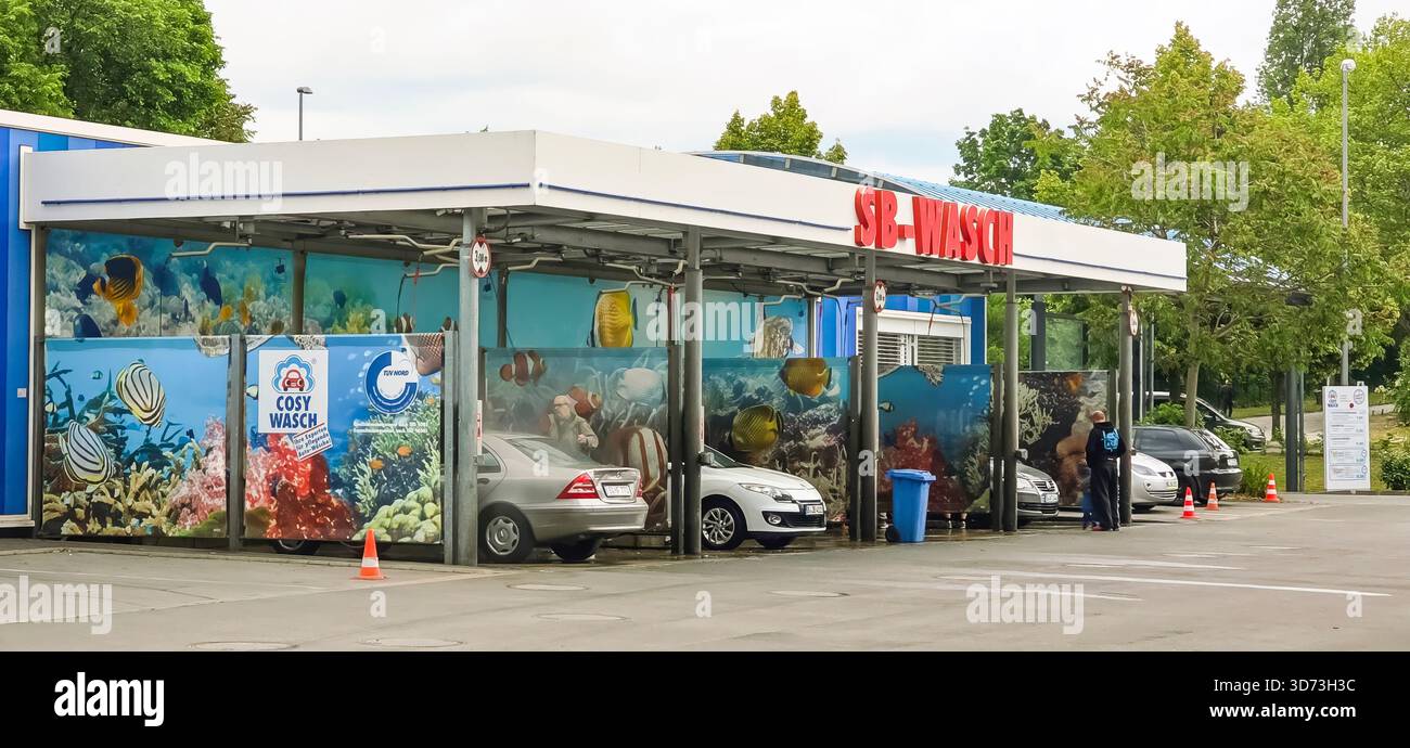 Berlin, Deutschland - 18. Mai 2025: Die Waschanlage zeigt ein farbenfrohes Unterwasserbild mit geparkten Fahrzeugen und Kunden in der Nähe. - Smartphone-aufgenommenes Stockfoto