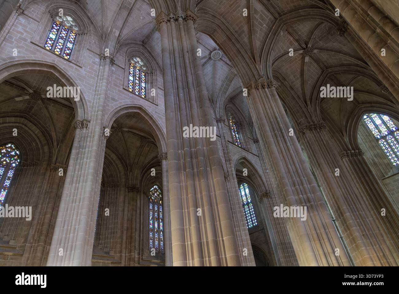 Majestätisches Inneres des Batalha-Klosters in Portugal. Hohe gotische Rippengewölbe, hoch aufragende Säulen und bunte Buntglasfenster. Stockfoto