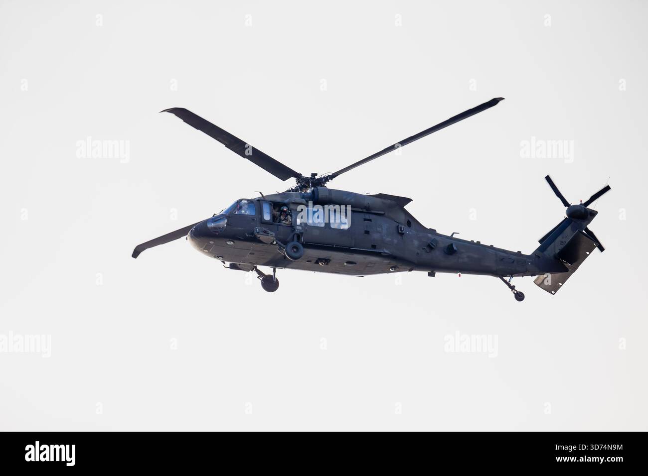 Militärhubschrauber in der Luft mit verlängertem Fahrwerk, Frontsensoren und Heckrotor sichtbar während des Flugbetriebs gegen hellen Himmel Stockfoto